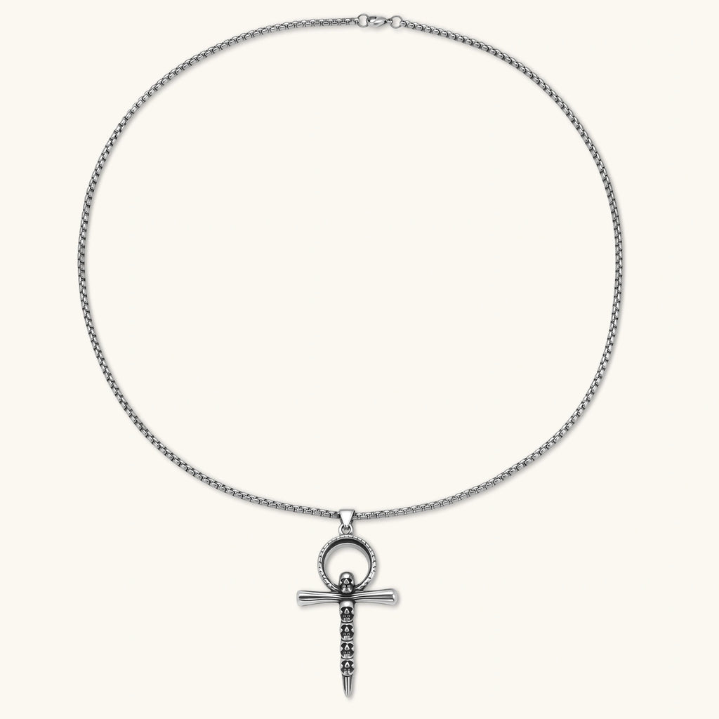 Silver stainless steel ankh pendant with skull motifs on vertical bar and textured ring top, on a box chain necklace.
