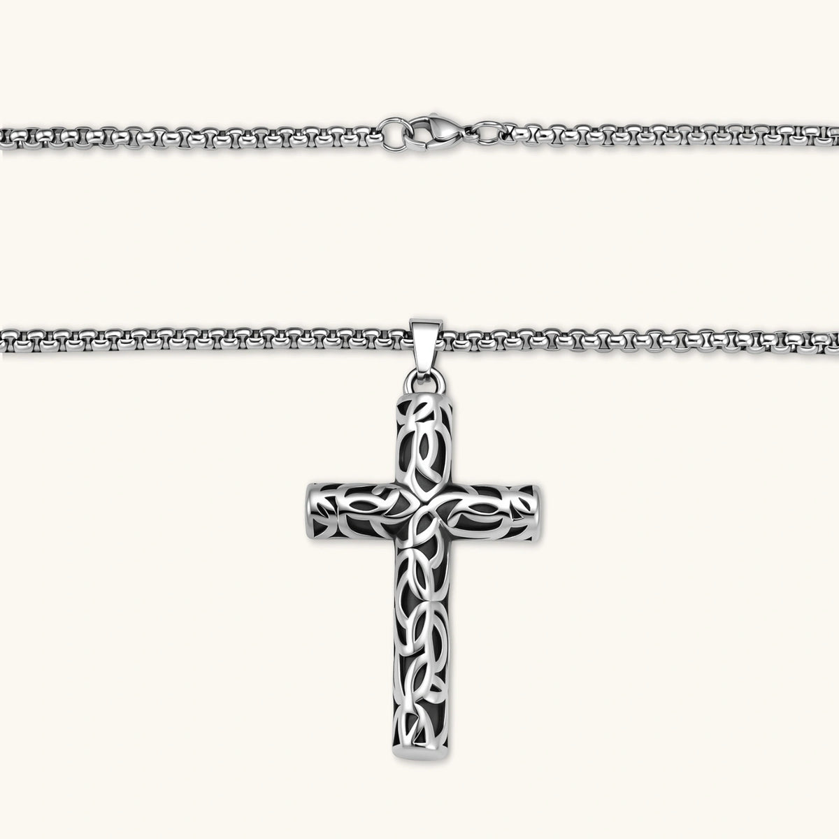 Silver stainless steel Celtic cross pendant with filigree vine pattern on a box chain, against a cream background.