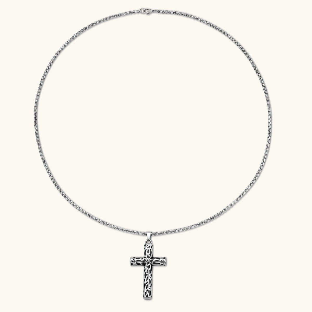 Silver stainless steel Celtic cross pendant with filigree vine pattern on a box chain, against a cream background.